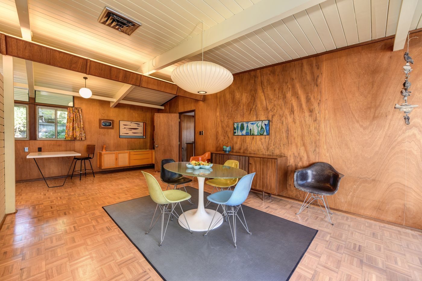 A mid-century dining area with wood walls and a beamed ceiling