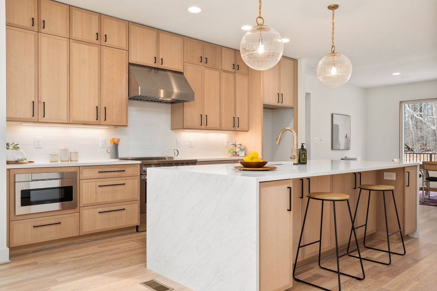 A kitchen with light wood cabinets, a stone island and pendant lighting