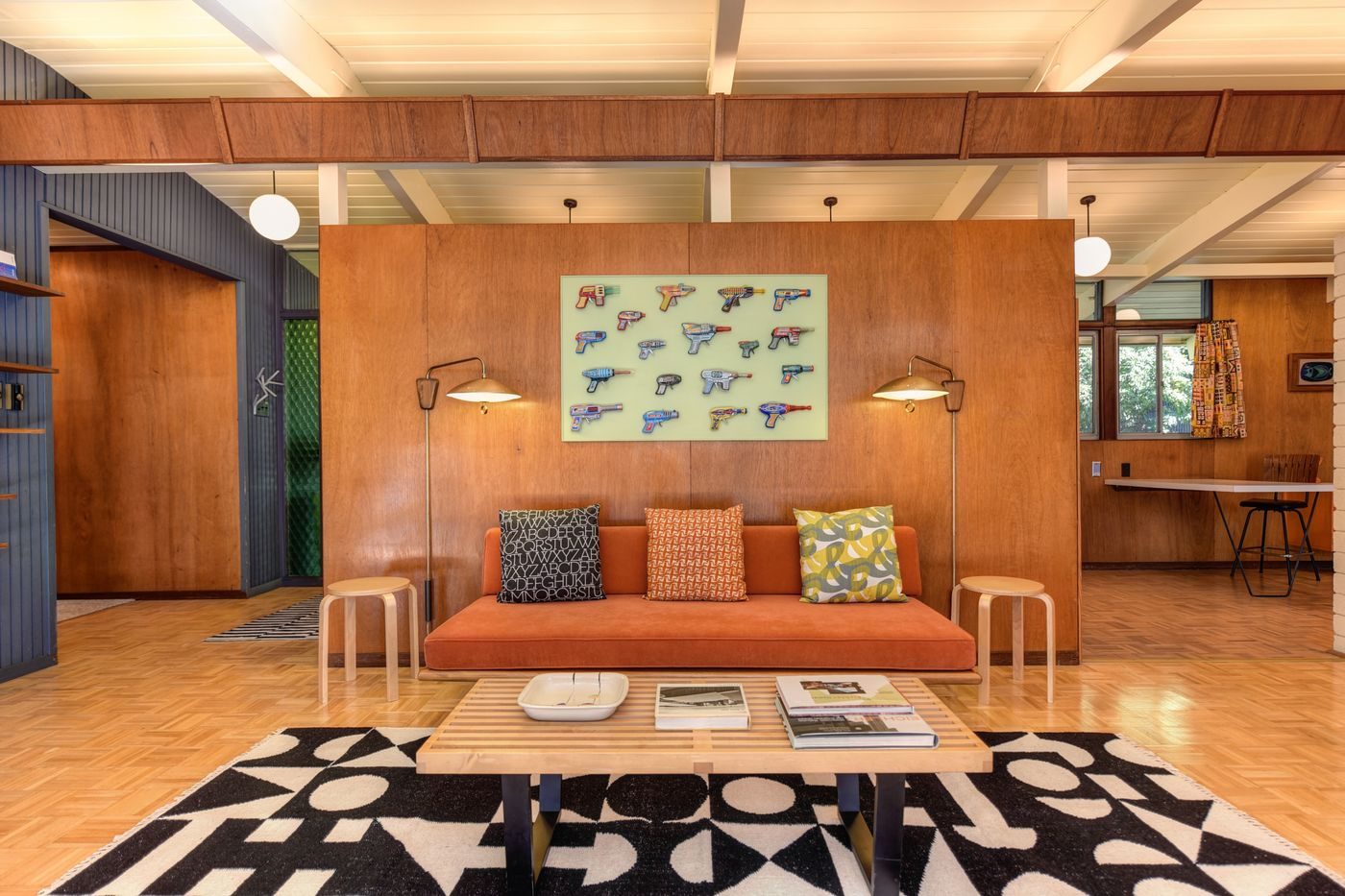 A wood-panelled living room with a low orange sofa and a bold graphic rug